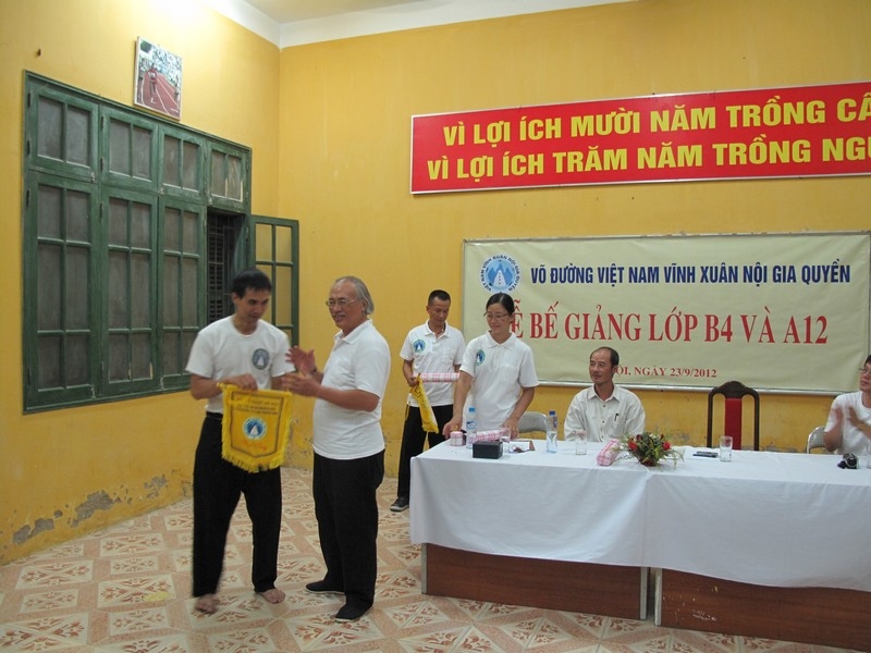Võ sư trưởng Nguyễn Ngọc Nội tặng huấn luyện viên Nhữ Tuấn Anh, huấn luyện viên lớp A12, cờ kỷ niệm của võ đường